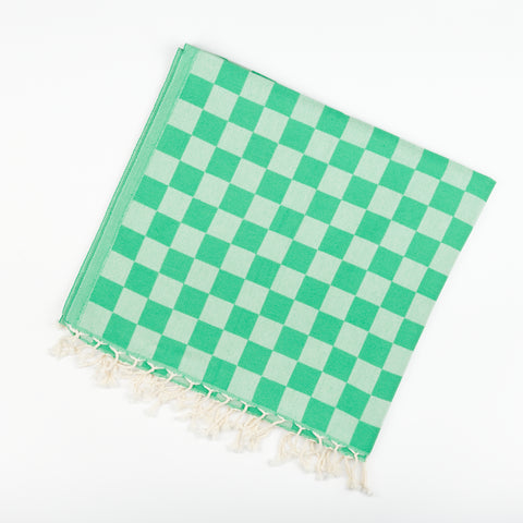 A square folded Turkish beach and bath towel by State the Label with a checkerboard pattern in two shades of green