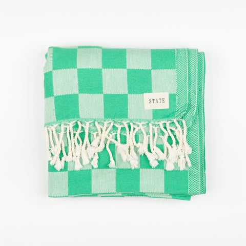 a folded green checkerboard towel with tassels and a small tag that reads State