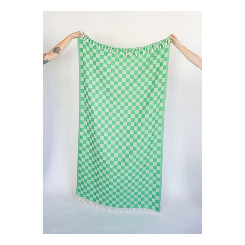 two arms holding up a bath towel with tassels and a green checkerboard pattern