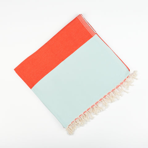A square folded Turkish beach and bath towel by State the Label in red and light blue