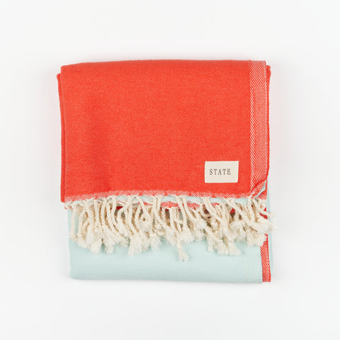 a folded red and light blue towel with tassels and a small tag that reads State