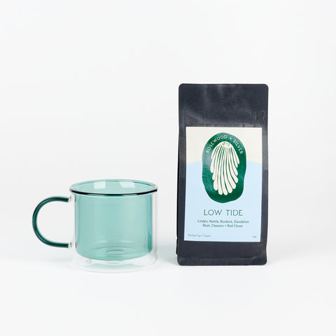 A Poketo Double Wall Mug in Teal next to a black bag of Rosewood + Silver Tea called Low Tide with a light blue and cream colored label