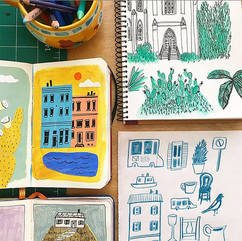 a table full of open sketchbooks with illustrated drawings of buildings, plants, a house and birds by artist Kristen Solecki