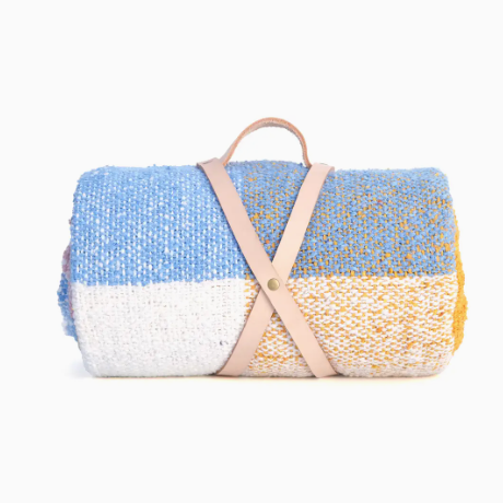 Rolled-up multicolored blanket with a leather strap on a white background