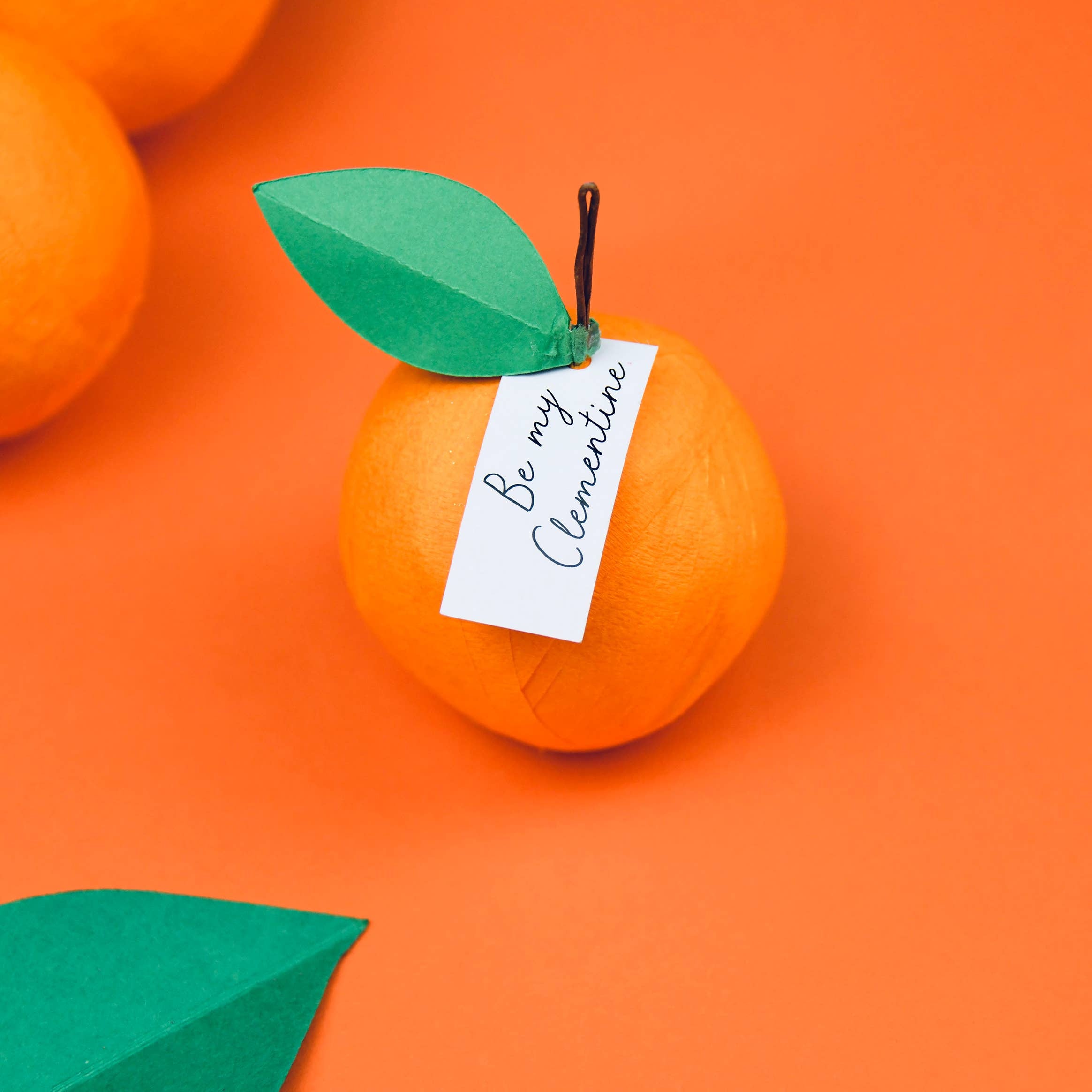 Orange surprise ball with a green leaf and 'Be my Clementine' tag on an orange background