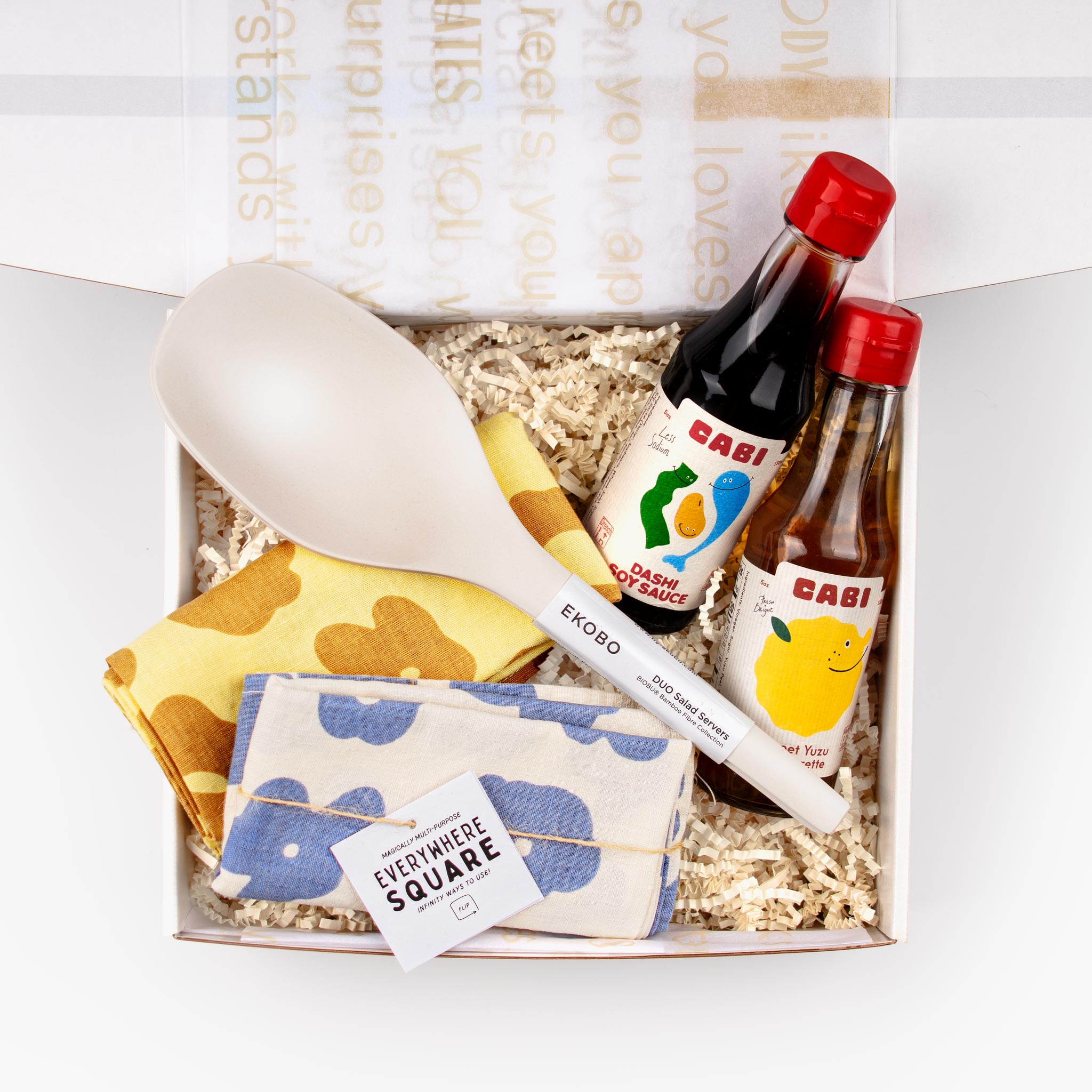 Overhead view of the Double Take Gift Set in an open gift box with Cabi condiments, folded textiles, and Ekobo servers.