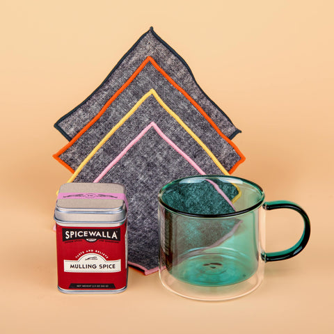 Mulling It Over gift set with teal double-walled Poketo glass mug, chambray Atelier Saucier napkins, and Spicewalla mulling spice tin on soft peach backdrop.