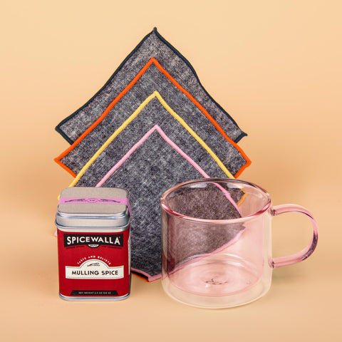 Mulling It Over gift set with pink double-walled Poketo glass mug, chambray Atelier Saucier napkins, and Spicewalla mulling spice tin on soft peach backdrop.