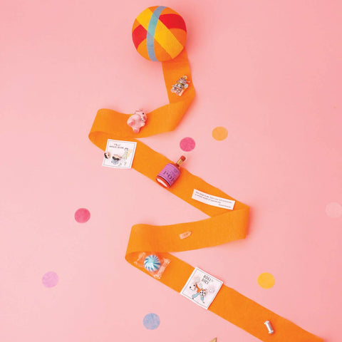 Orange surprise ball partially unwound with colorful toys and treats inside shown on a pink background