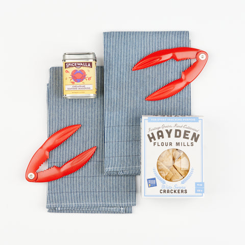 Tide to Table Gift Set items arranged together with Atelier Saucier tea towels, Spicewalla Chesapeake seasoning, Hayden Flour Mills crackers, and Fox Run lobster crackers