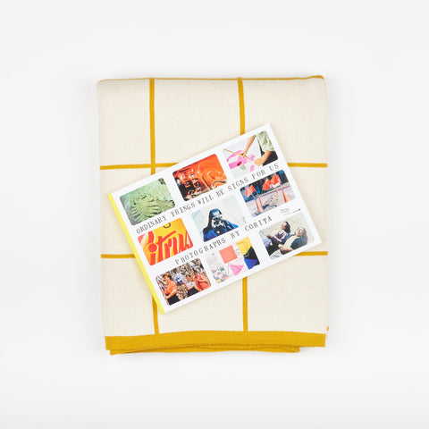 A Book and Blanket Gift set including DAP Artbook publication Ordinary Things Will-Be Signs For Us and a Sophie Home Cotton Knit Throw blanket with a citrus yellow grid