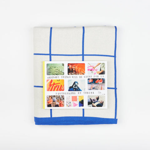 A Book and Blanket Gift set including DAP Artbook publication Ordinary Things Will-Be Signs For Us and a Sophie Home Cotton Knit Throw blanket with a cobalt grid
