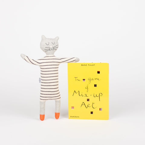 A Sophie Home stuffed animal toy cat in stripes standing and leaning on a copy of Phaidon Kids book The Game of Mix-Up Art a