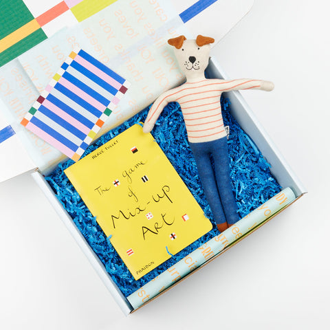 A Cette gift box showing Phaidon Kids book The Game of Mix-Up Art and a Sophie Home Kids stuffed animal toy dog in blue pants and red striped shirt